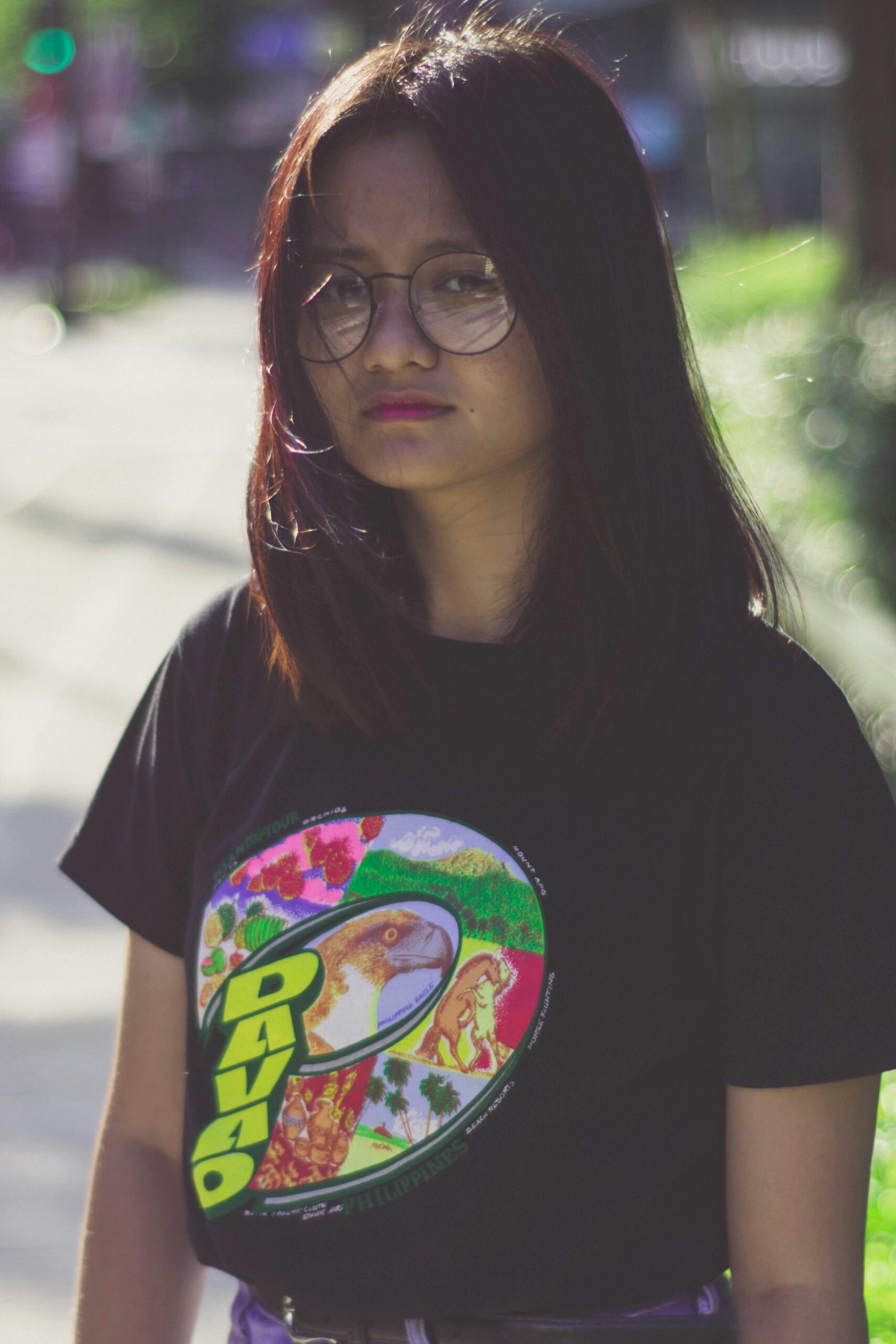 pexels photo 1752866 1752866 Portrait of a young woman wearing glasses and a graphic t-shirt, captured outdoors.