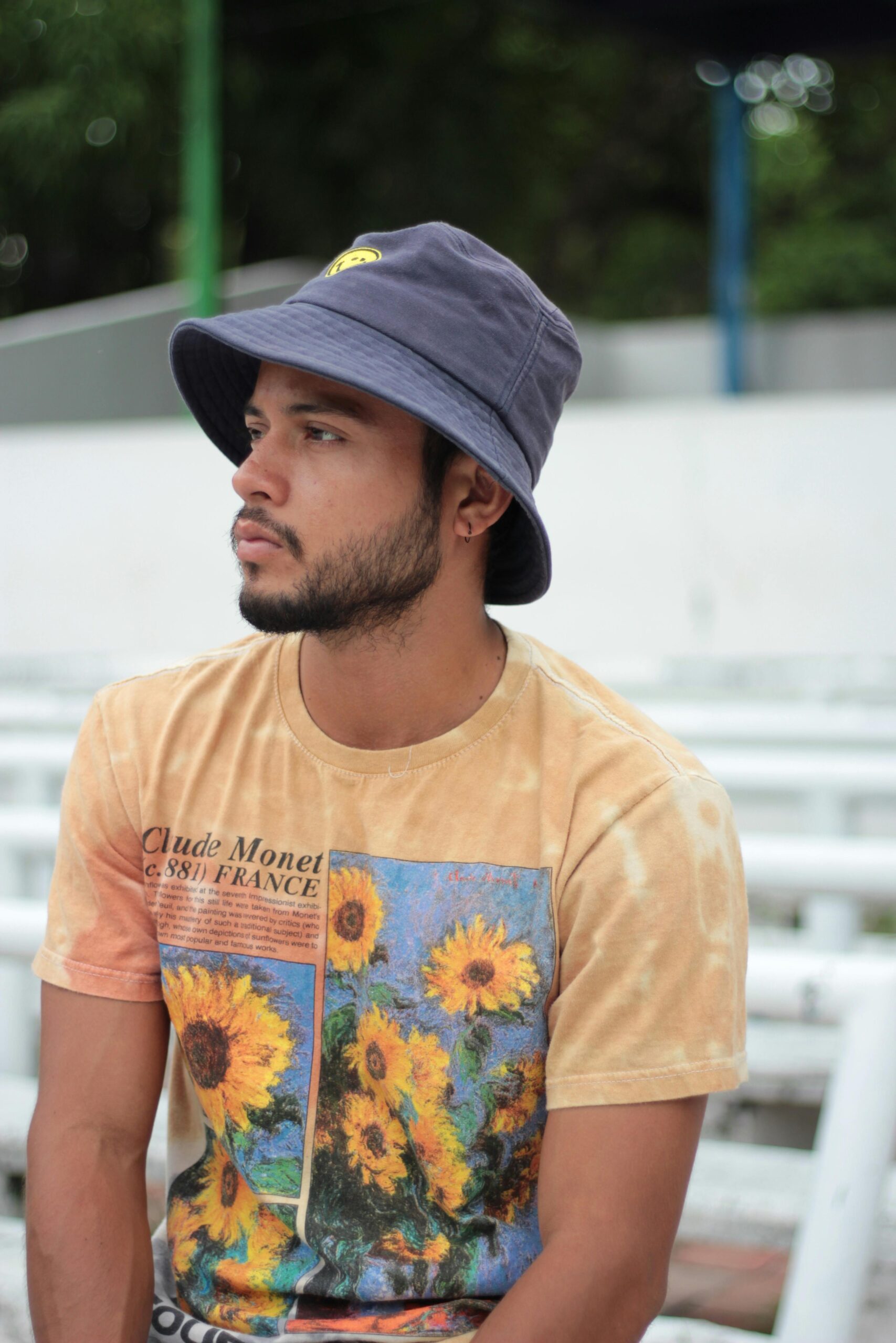 pexels photo 18835059 18835059 Young man in a sunflower tee and bucket hat sitting outdoors, evoking casual fashion vibes.