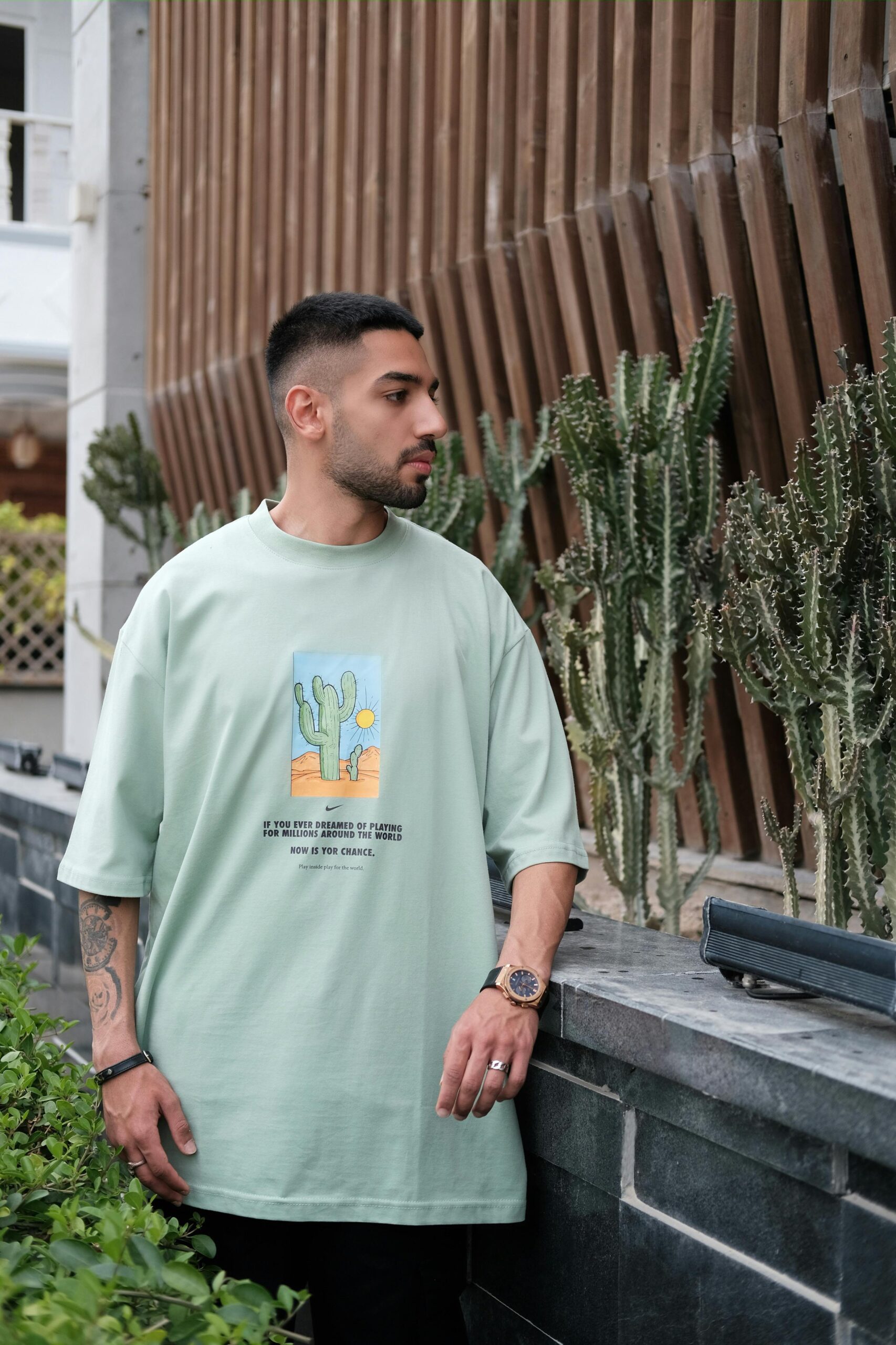 pexels photo 18856592 18856592 Stylish man in printed t-shirt posing by cacti in a modern setting.